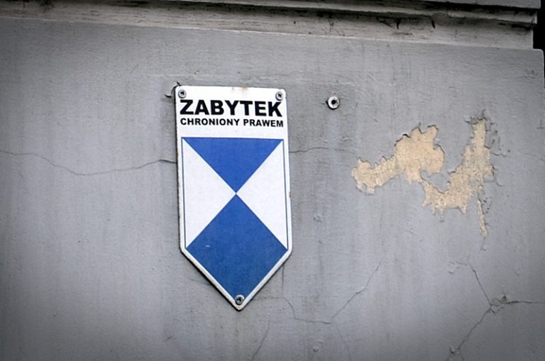 Obdrapana ściana budynku, na której wisi tabliczka z napisem zabytek