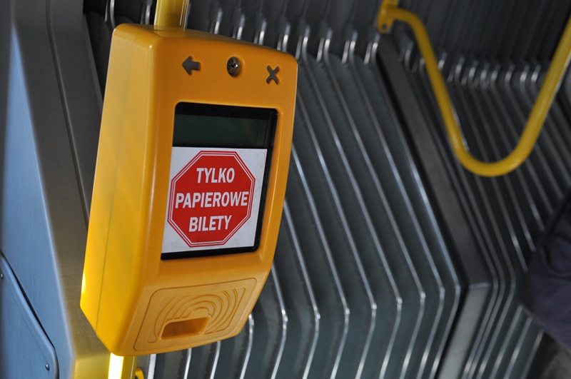 Żółty kasownik biletów komunikacji miejskiej, z czerwoną naklejką, na której jest napisane: Tylko bilety papierowe, stoi wewnątrz autobusu