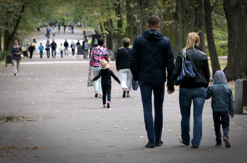 Para; kobieta i mężczyzna wraz z dzieckiem idą główną aleją przez Park Planty. Para jest uchwycona od tyłu
