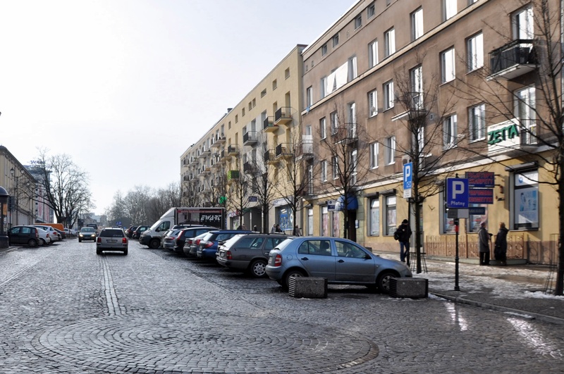 Ulica, przy której stoi blok oraz znajdują się zaparkowane samochody