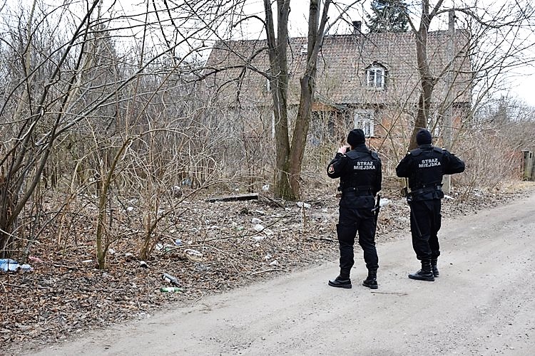 Dwóch funkcjonariuszy Straży Miejskiej stoi przed starym budynkiem