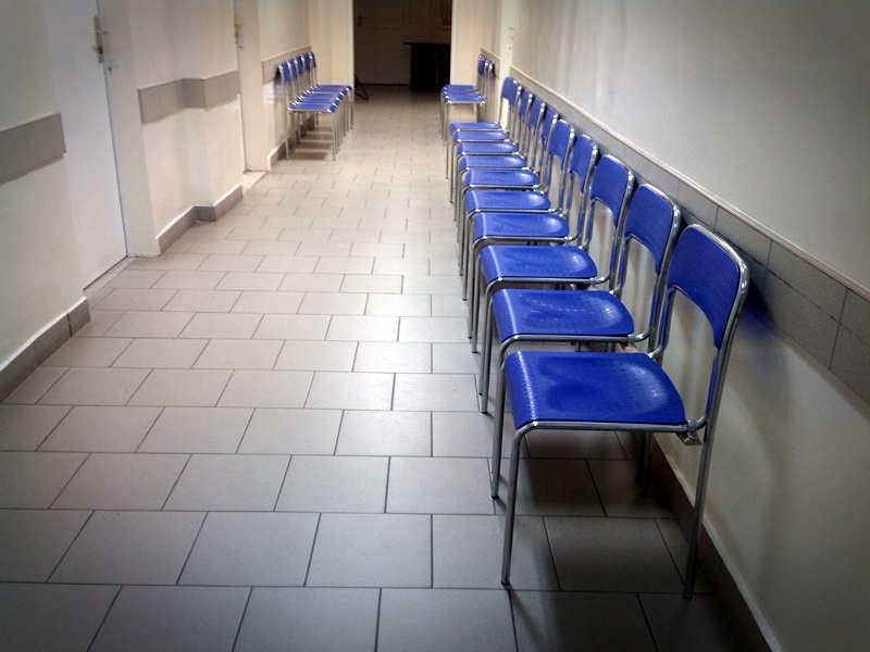 Korytarz w przychodni. Po prawej stronie stoi rząd niebieskich, plastikowych krzeseł