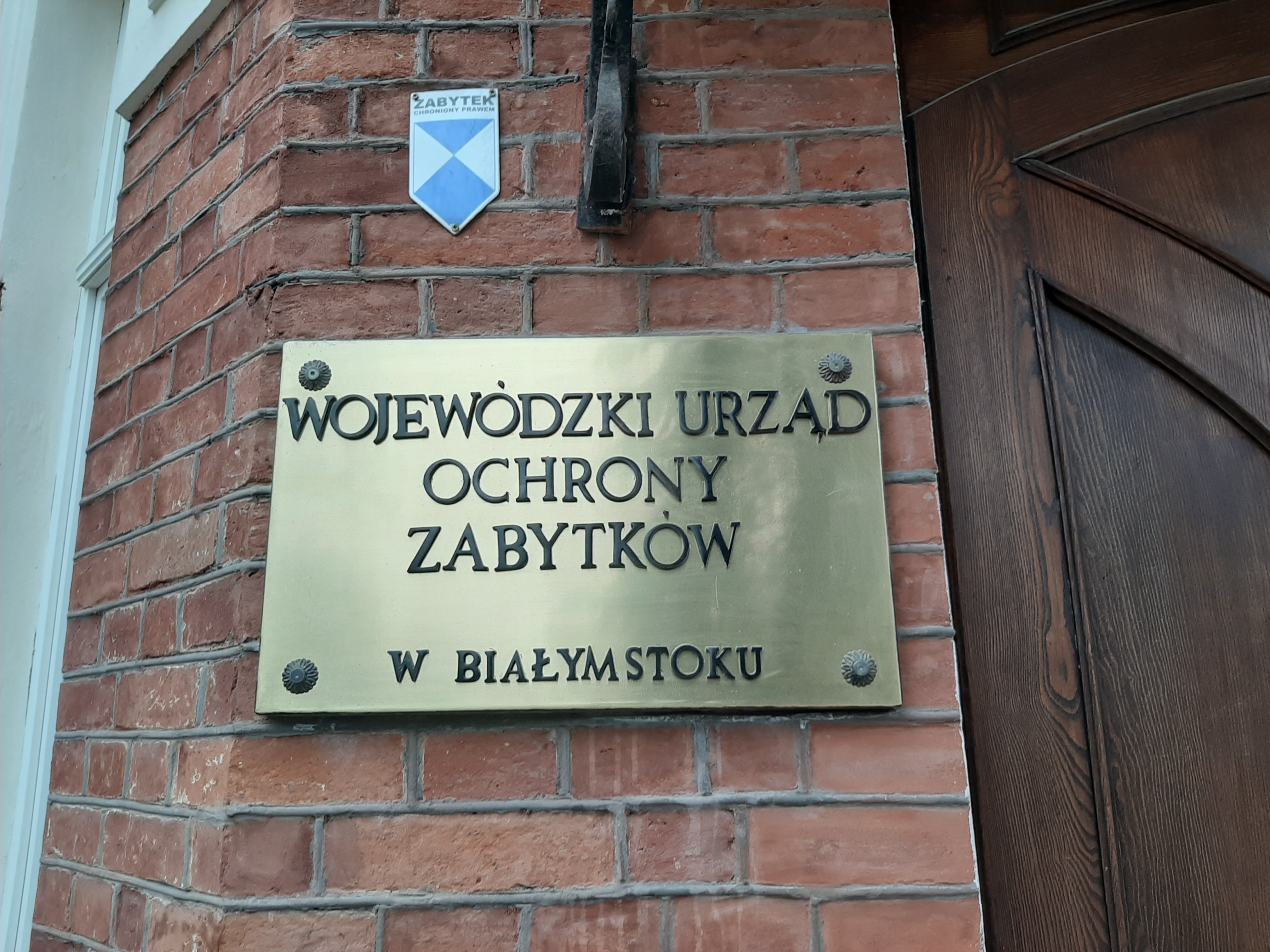 Ceglana ściana a na niej złota tabliczka z napisem Wojewódzki Urząd Ochrony Zabytków