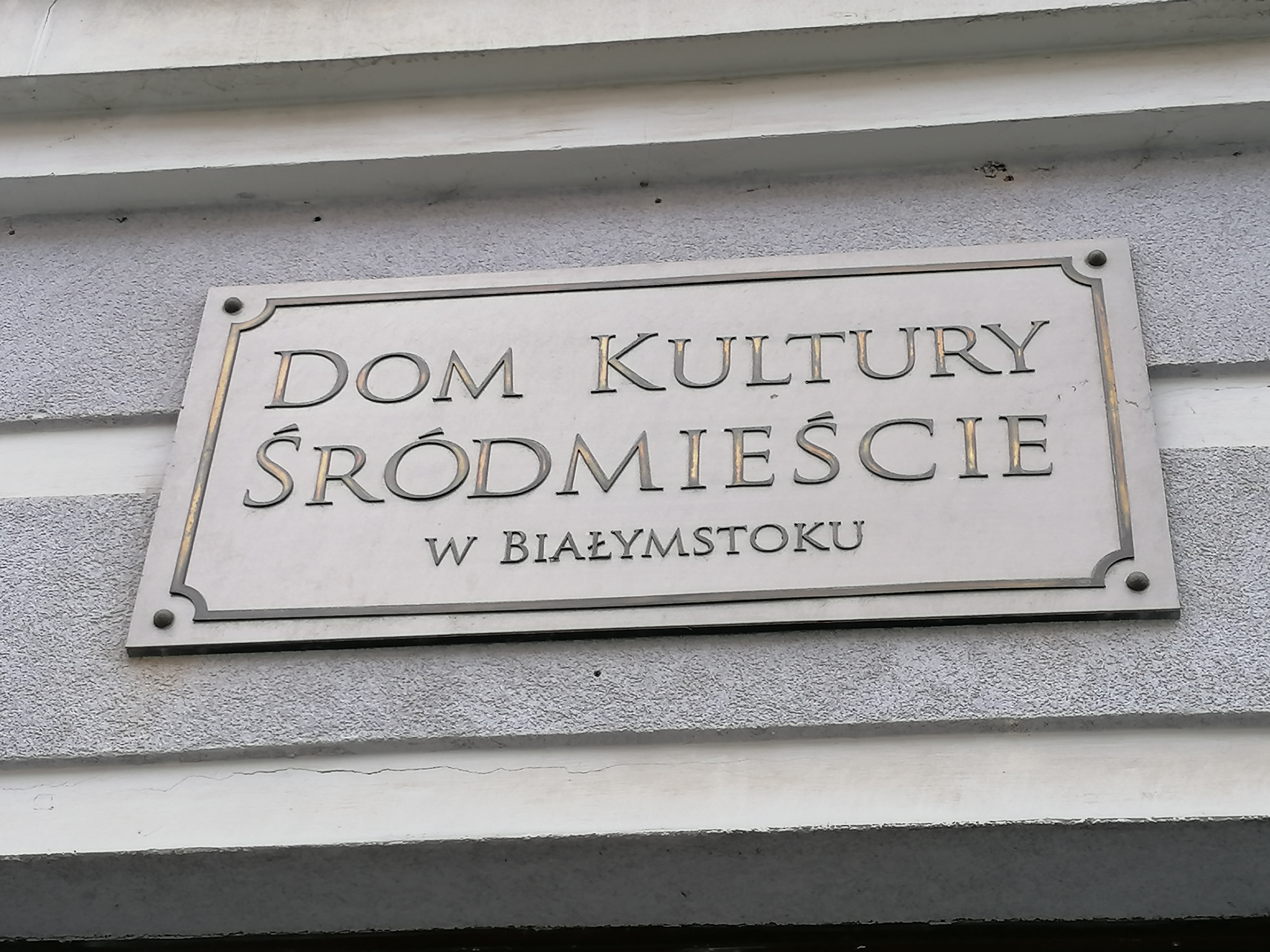 Szara tabliczka z napisem: Dom Kultury Śródmieście w Białymstoku
