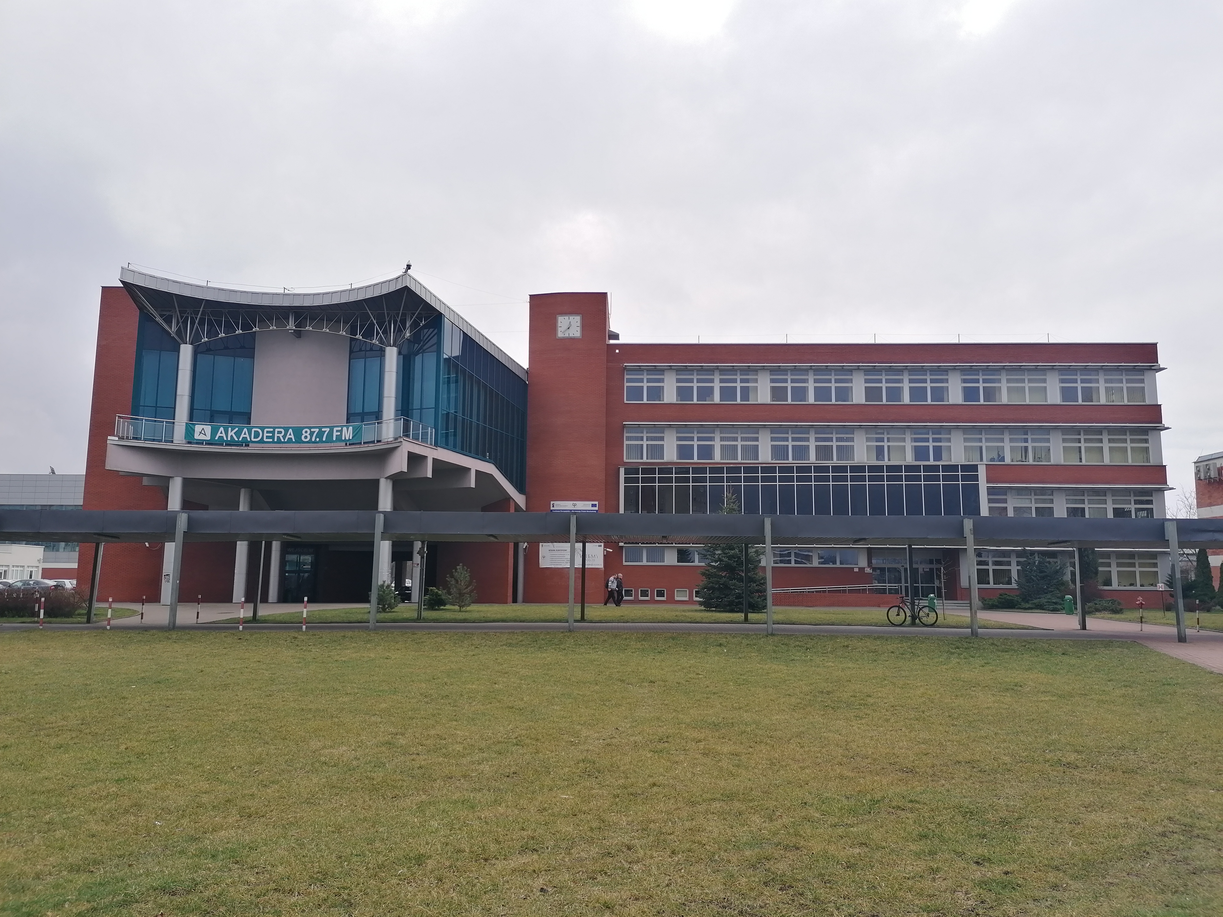 Zdjęcie budynku. Na pierwszym planie jest trawnik. W oddali widać budynek z czerwoną elewacją