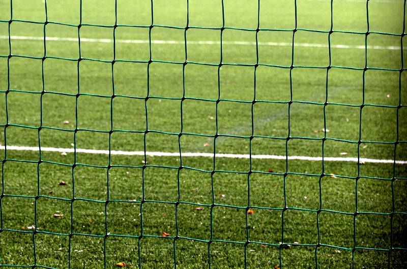 Siatka bramki piłkarskiej. W tle widać zieloną murawę stadionu.
