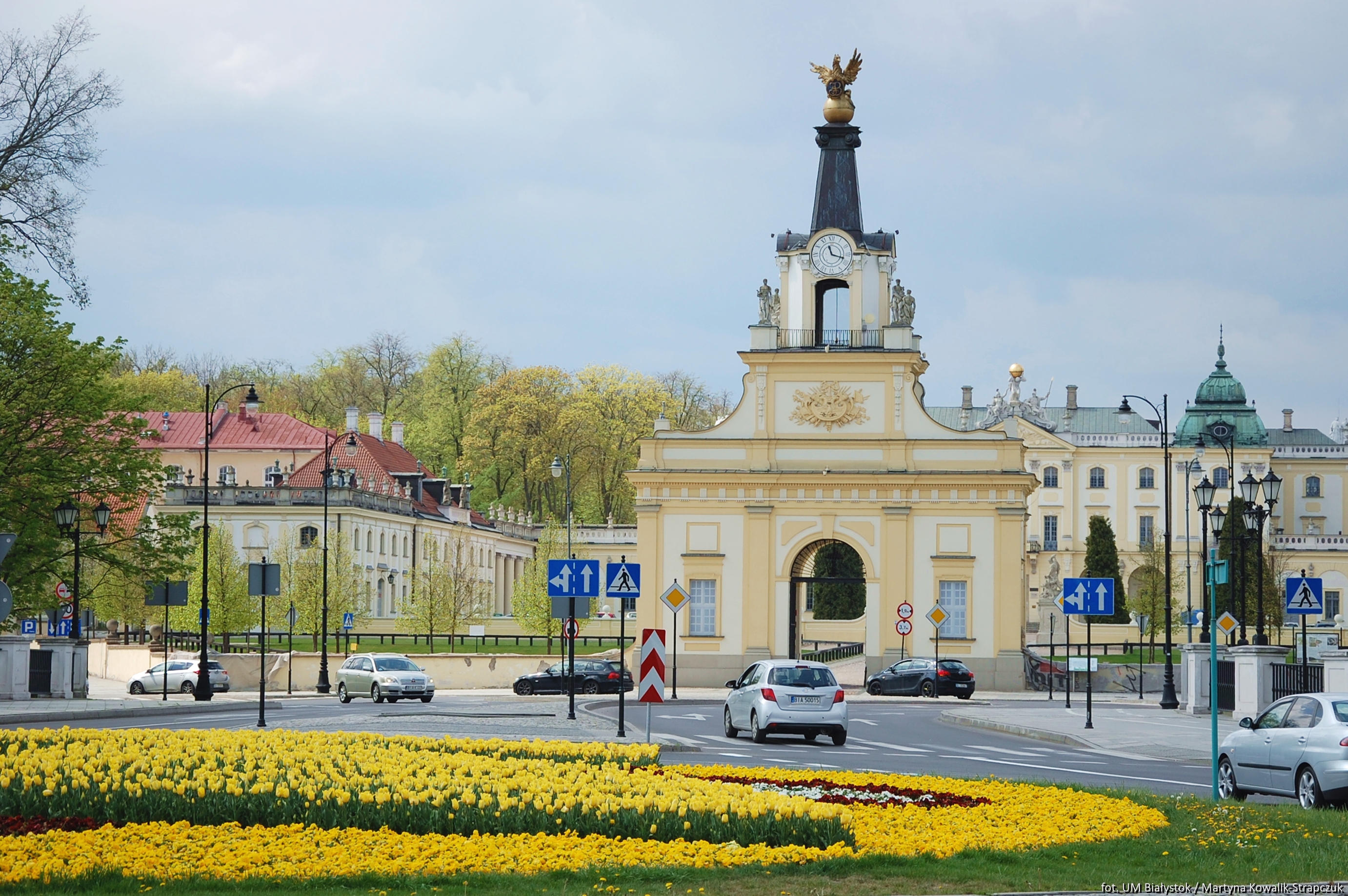 Brama Pałacu Branickich widziana za rondem obsadzonym kolorowymi kwiatami.