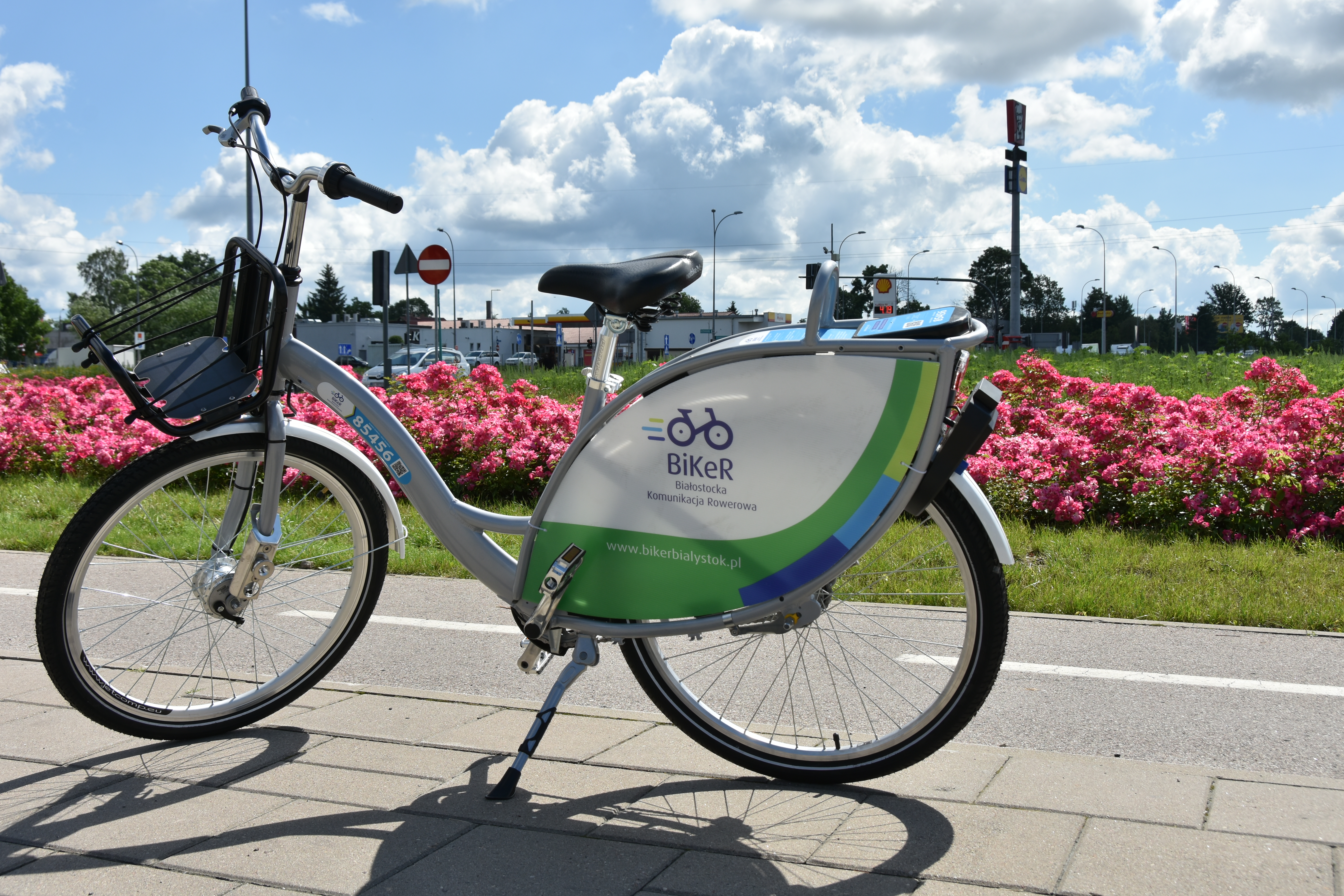 Rower miejski stoi na chodniku, w tle kolorowe kwiaty