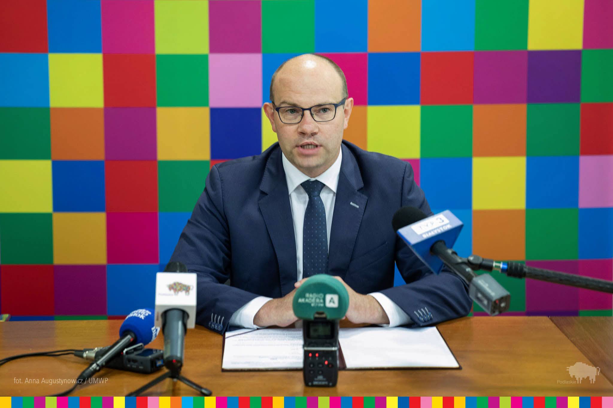 Marszałek Artur Kosicki siedzi na tle ścianki, w kolorowe kwadraty