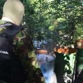 Funkcjonariusze KAS stoją na terenie leśnej bimbrowni. Na miejscu jest kadź zawierająca 300 litrów fermentującego zacieru, chłodnica i kocioł, a także doły z wodą wykorzystywaną w wytwarzaniu bimbru oraz rozlewisko
