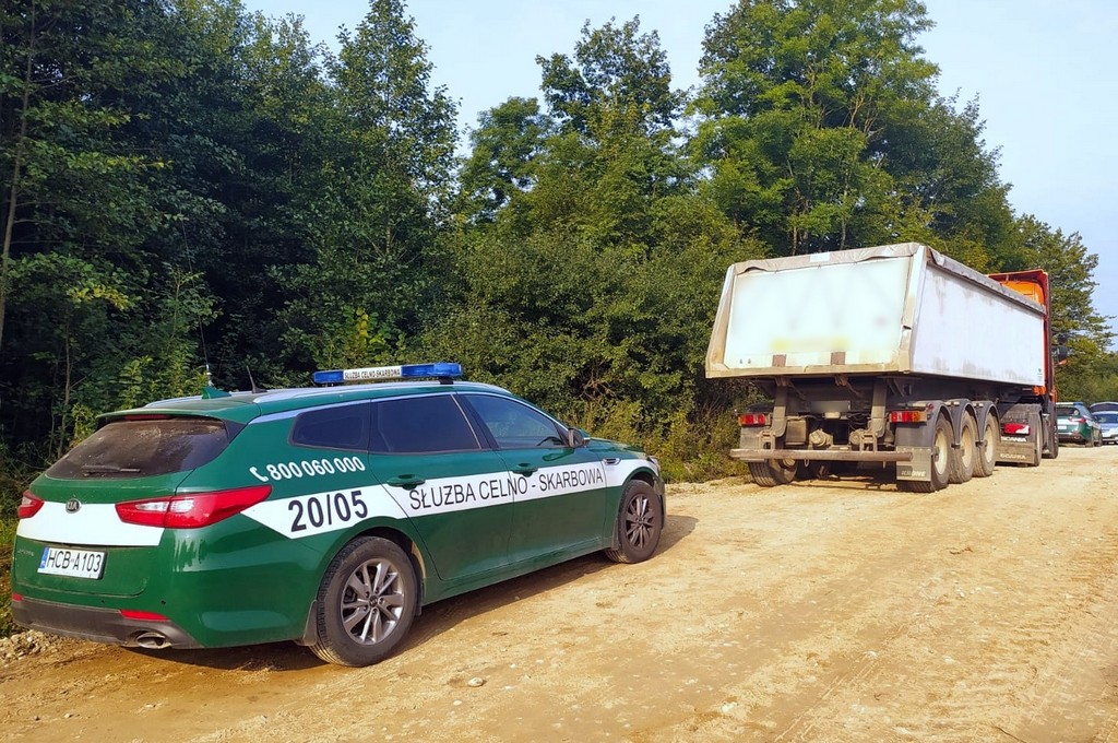 Na szutrowej drodze stoi zatrzymana po pościgu wywrotka z nielegalnymi papieorsami i samochód służbowy KAS.