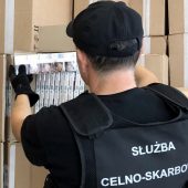 Funkcjonariusz KAS wyjmuje z kartonowego pudełka karton papierosów z przemytu