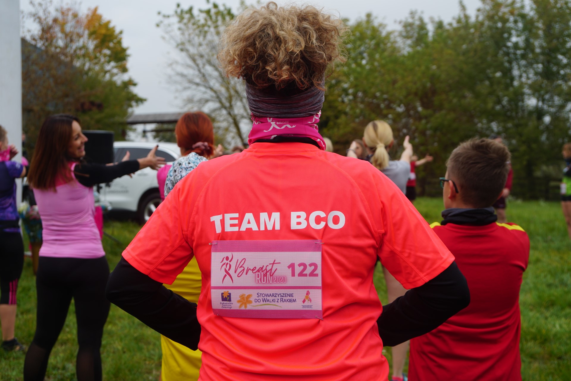 Kobieta stoi odwrócona tyłem. Ma na sobie czerwoną koszulkę z napisem TEAM BCO.