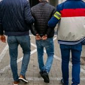Policjanci trzymają skutego kajdankami mężczyznę.