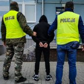 Policjanci trzymają skutego kajdankami mężczyznę.