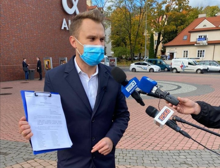 Mężczyzna stoi w maseczce przed galerią handlową. Mówi do mikrofonów dziennikarzy.