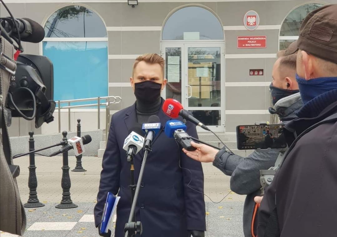 Poseł Krzysztof Truskolaski przemawia do mikrofonu na konferencji prasowej przed siedzibą komendy wojewódzkiej policji.