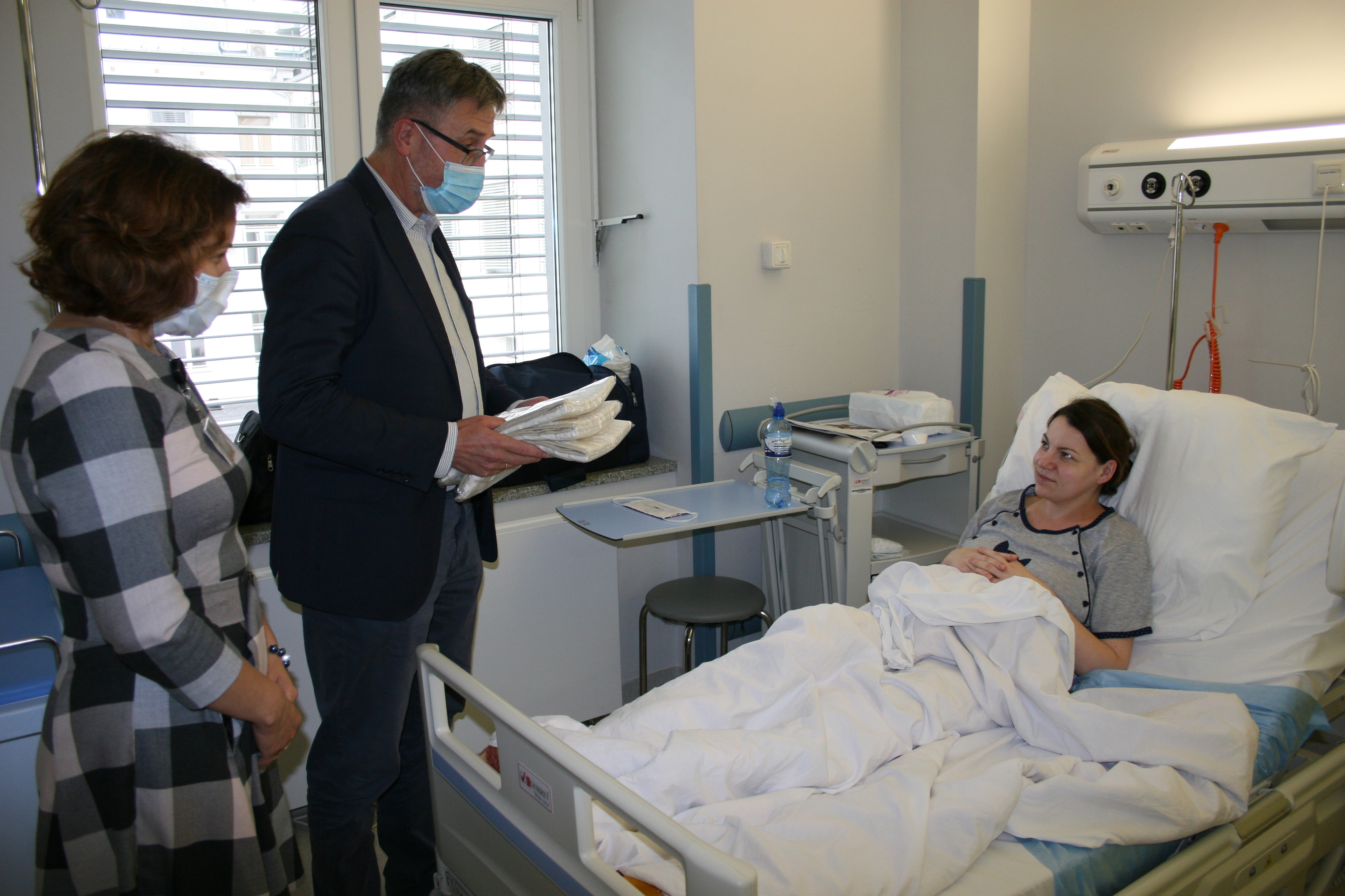 Świeżo upieczona mamy trojaczków leży w łóżku szpitalnym. Z wizytą i prezentami dla dzieci przychodzi do niej dyrektor szpitala klinicznego.