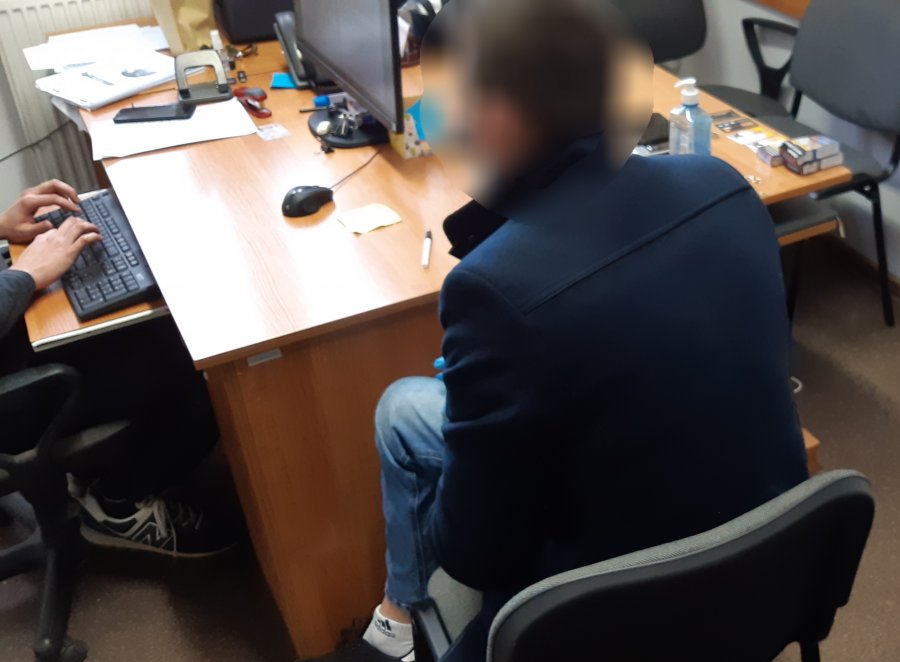 Przy policyjnym biurku siedzi mężczyzna. Trwa jego przesłuchanie.