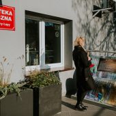 Kobieta stoi przed budynkiem biblioteki i ogląda eksponat w kształcie ławki
