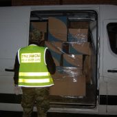 Pogranicznik stoi przy otwartych drzwiach busa. W przestrzeni ładunkowej widać kartony wypełnione papierosami z przemytu
