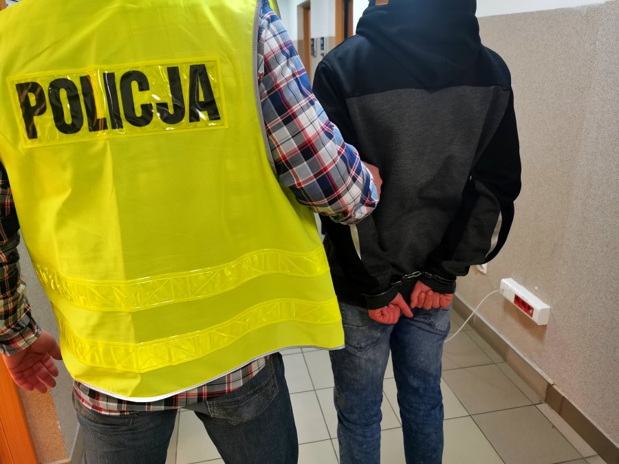 Policjant trzyma skutego kajdankami mężczyznę