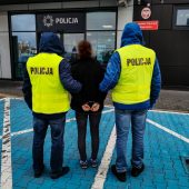Policjanci trzymają skutą kajdankami kobietę