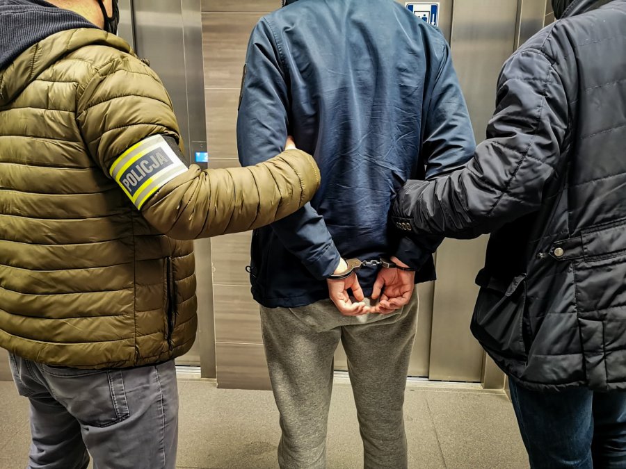 Dwaj policjanci trzymają skutego kajdankami mężczyznę