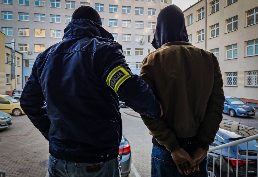 Policjant trzyma skutego kajdankami mężczyznę