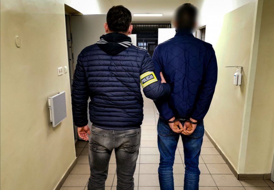 Policjant trzyma skutego kajdankami mężczyznę