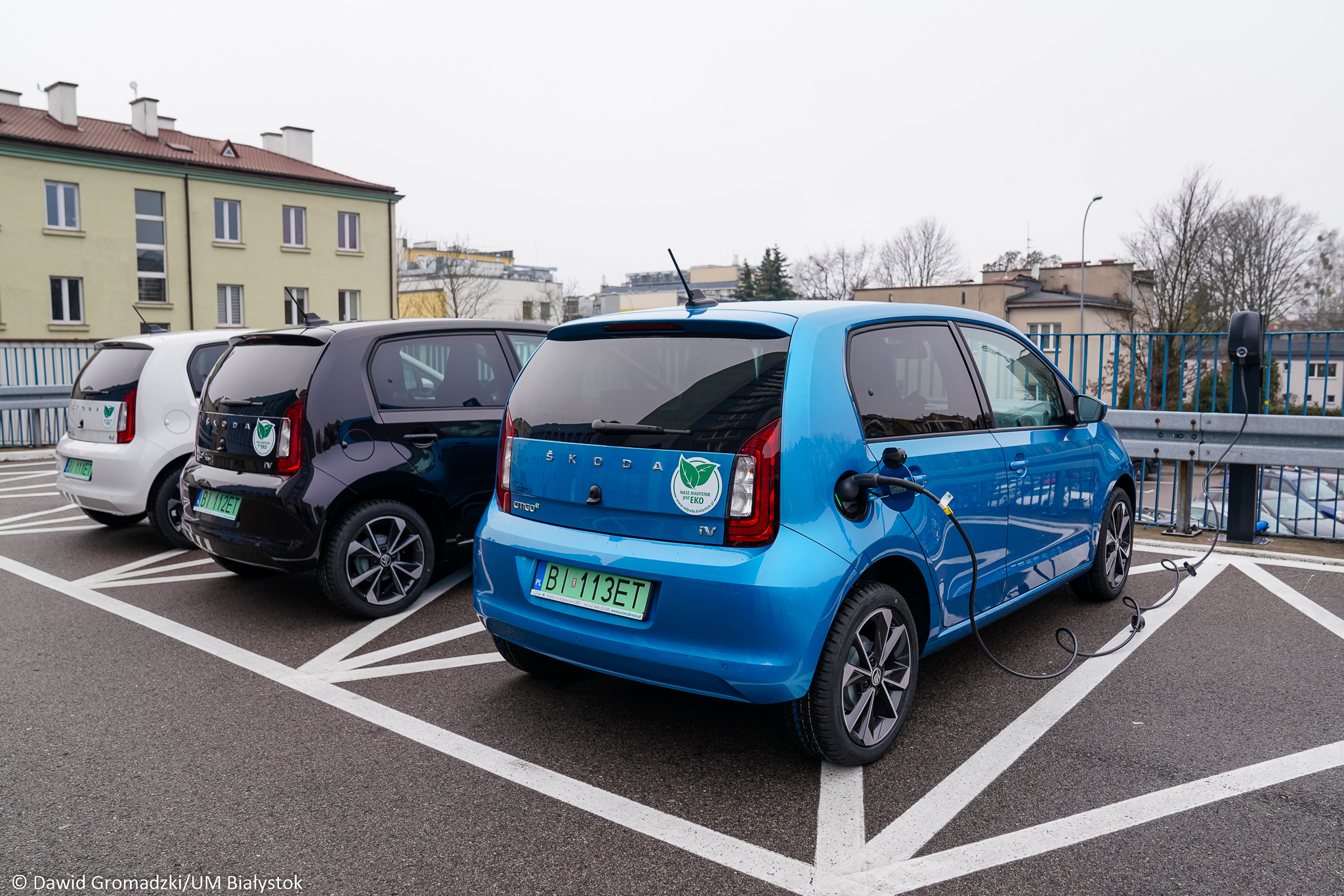 Na parkingu za Urzędem Miejskim w Białymstoku przy ul. Słonimskiej stoją trzy auta elektryczne. Od lewej strony stoi samochód biały, pośrodku czarny, z prawej niebieski