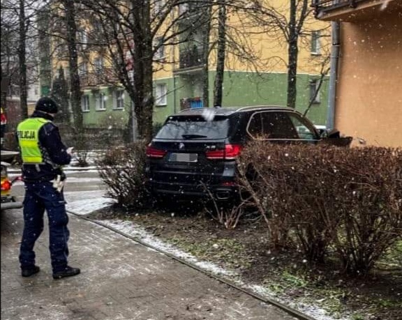 Policjant stoi przy samochodzie, który wjechał na chodnik potrącając dwie osoby