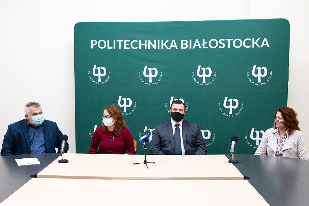 Na tle zielonej ścianki Politechniki Białostockiej siedzą cztery osoby