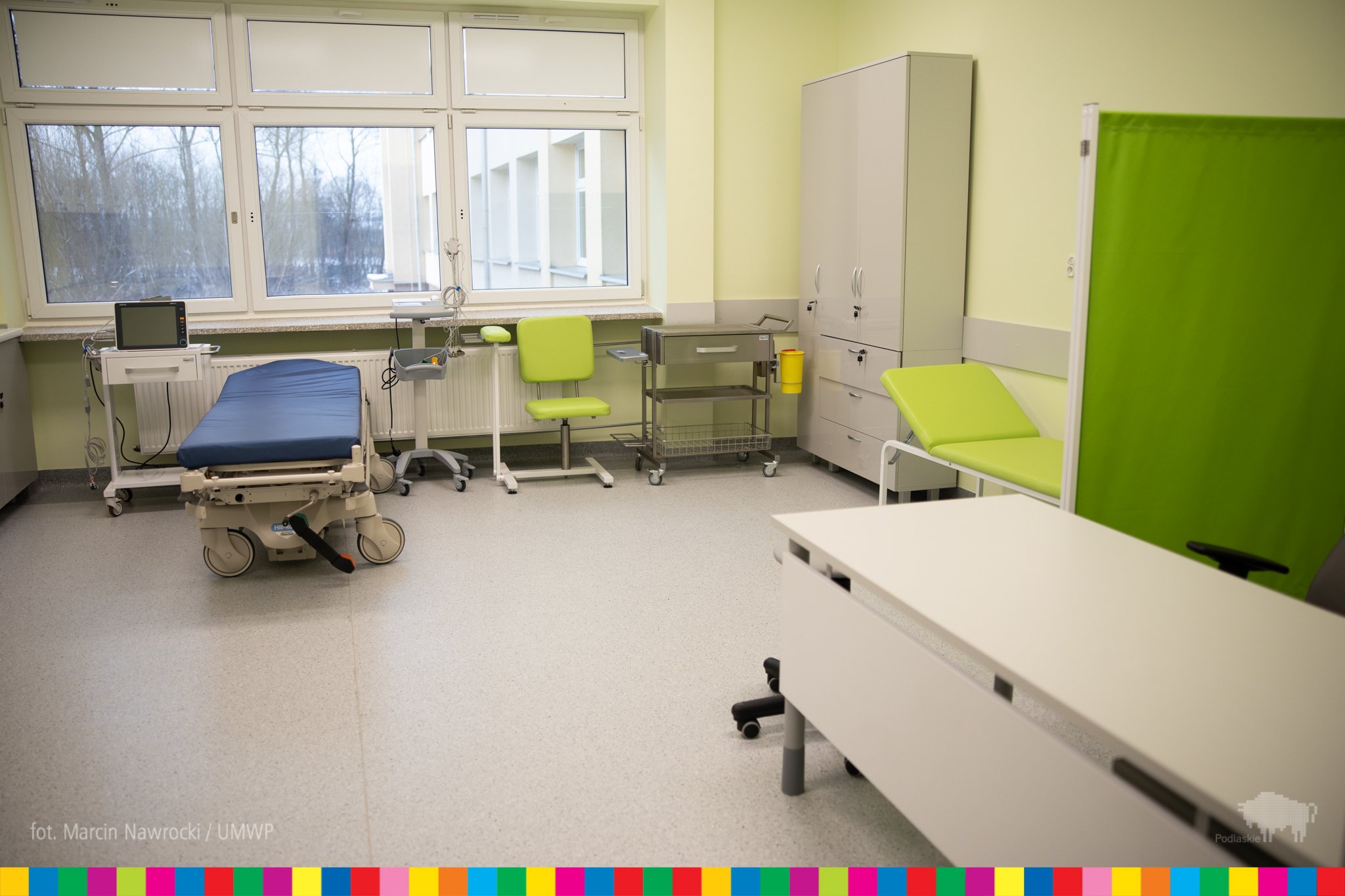 Sala szpitala. Pomieszczenie jest jasne, z zielonymi dodatkami. Po prawej stronie soi łóżko szpitale, na wprost jest okno pod którym stoi kolejne łóżko