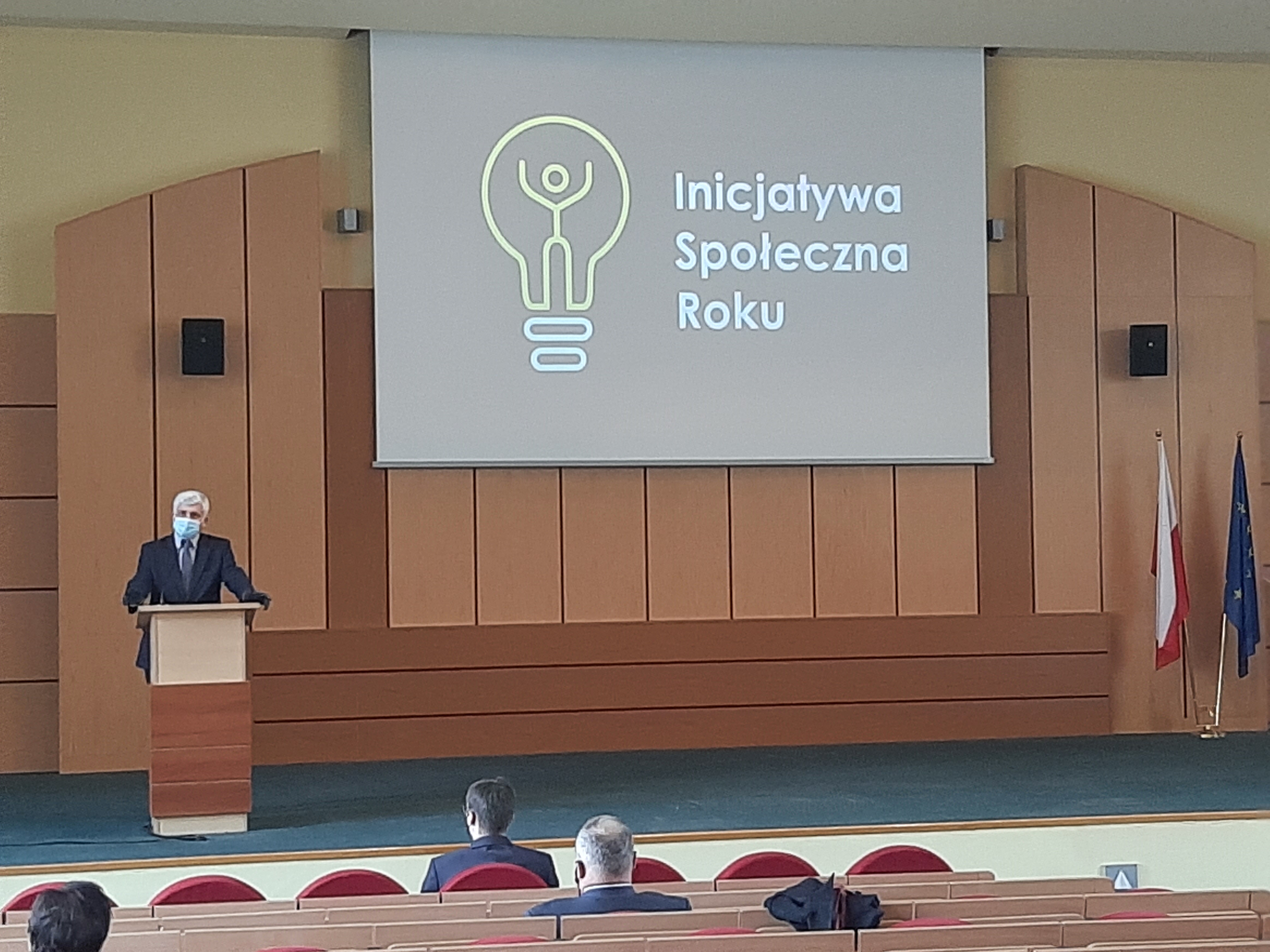 Sala konferencyjna Podlaskiego Urzędu Wojewódzkiego. Przy mównicy stoi wojewoda. Na ścianie znajduje się rzutnik, na którym jest wyświetlony napis Inicjatywa Społeczna Roku