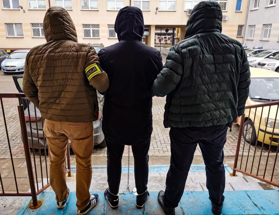 Dwaj policjanci trzymają pod ramię skutego kajdankami mężczyznę