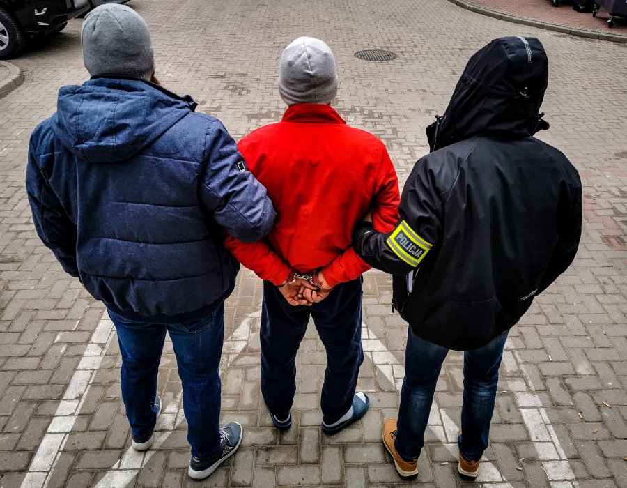 Dwaj policjanci trzymają skutego kajdankami mężczyznę