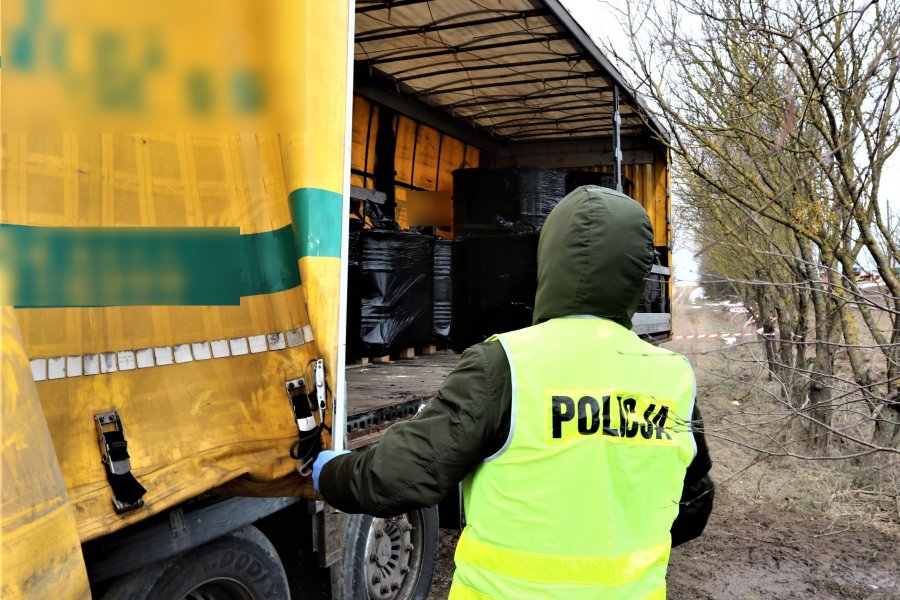 Funkcjonariusz policji stoi przy ciężarówce wypełnionej beczkami z płynem niewiadomego pochodzenia