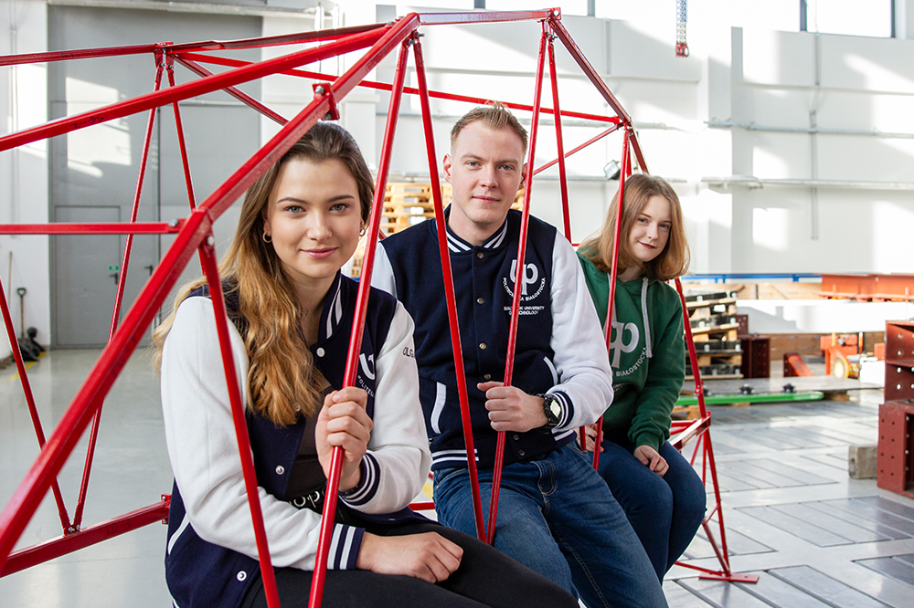 Troje studentów Politechniki Białostockiej siedzi ubranych w bluzy z logo uczelni