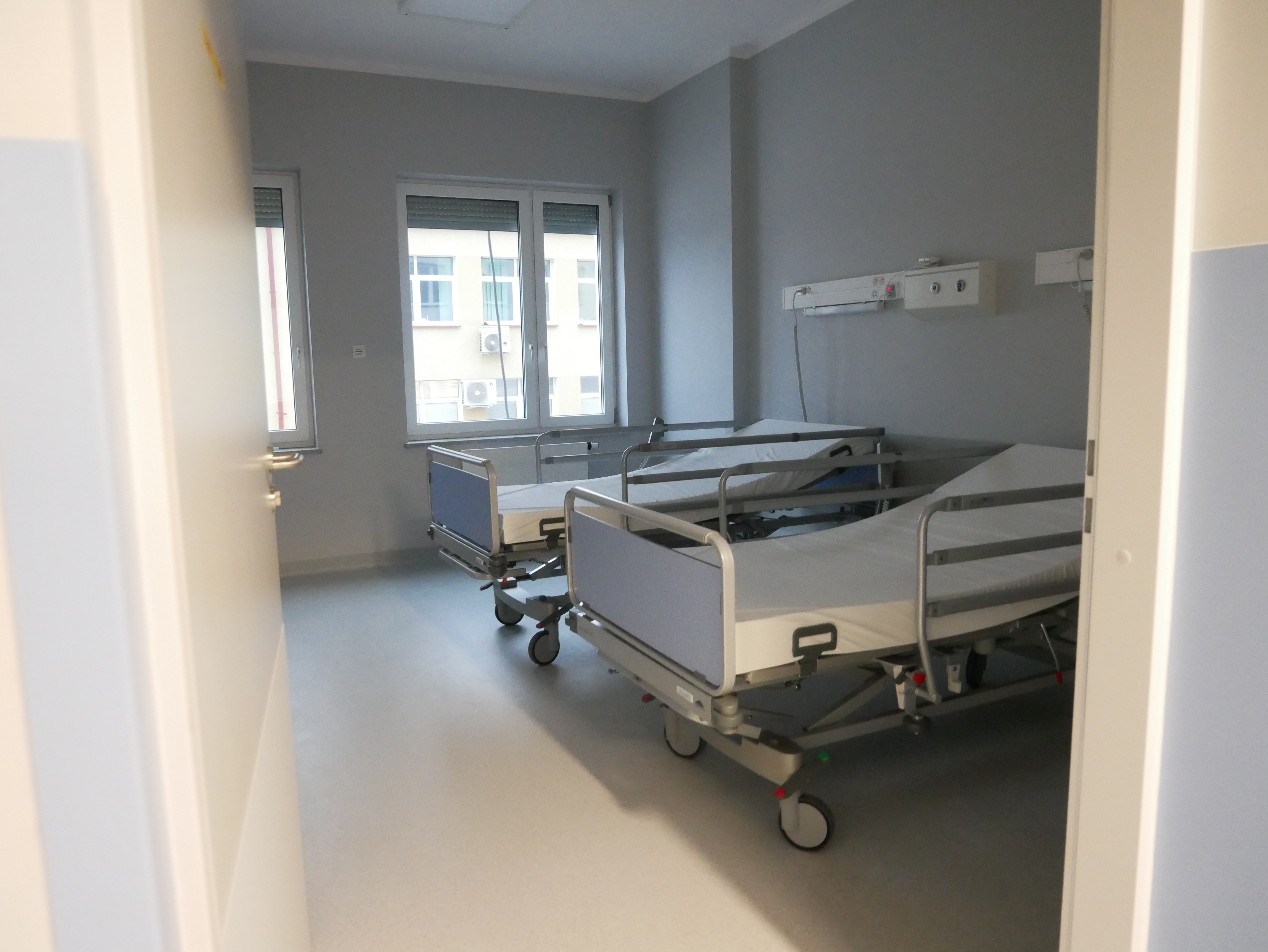 Sala szpitalna, w której stoją dwa łóżka. Na końcu sali jest okno