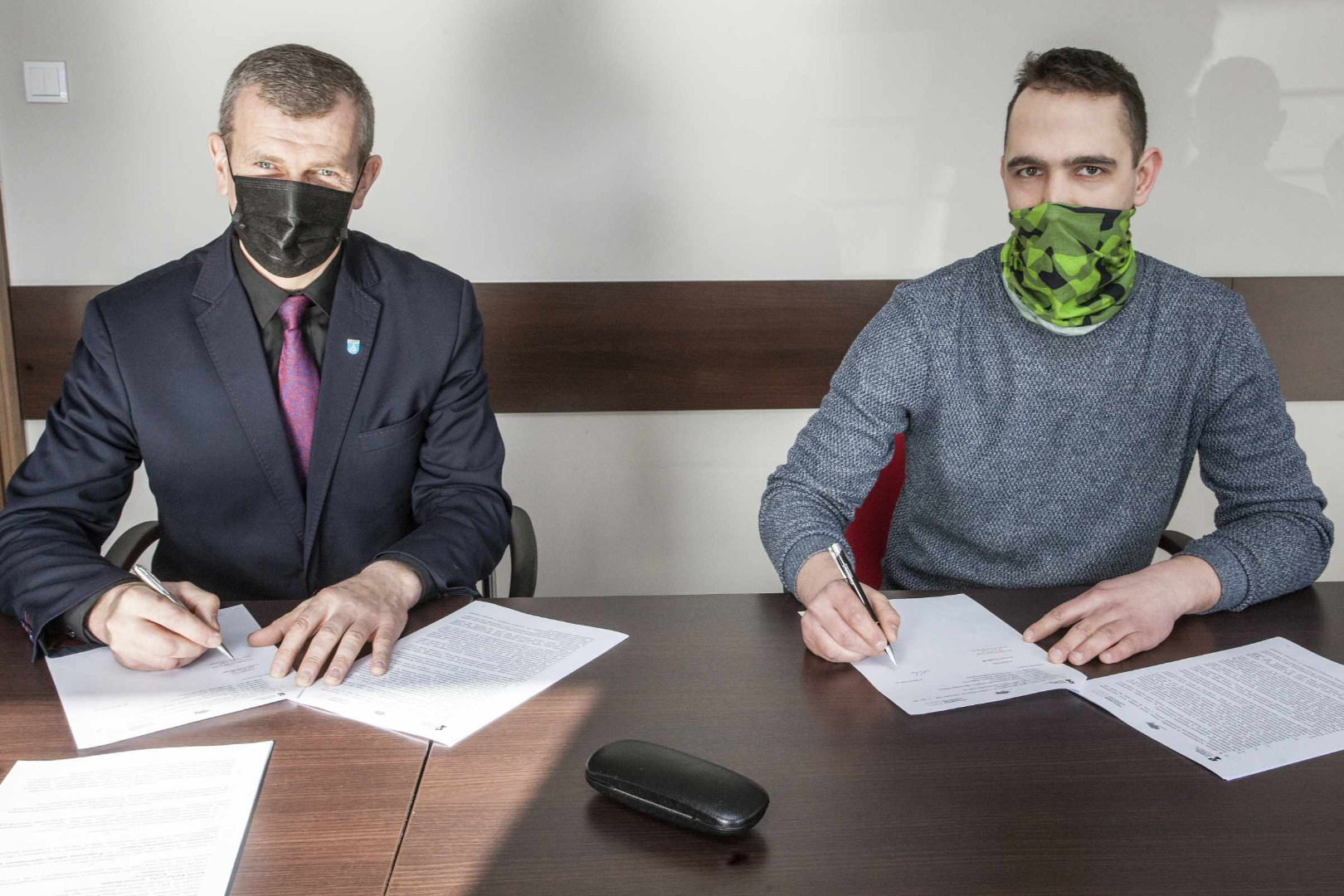 Przy stole siedzą dwaj mężczyźni podpisujący umowę o współpracy