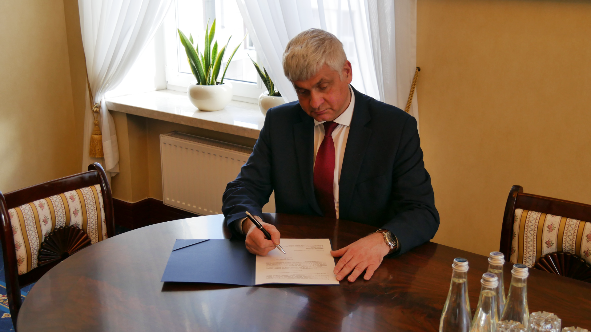 Wojewoda siedzi przy stole i podpisuje dokumenty