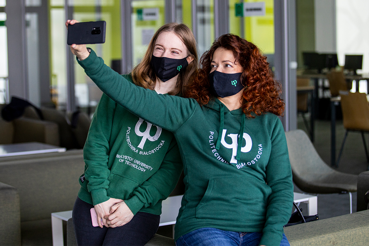 Dwie kobiety w zielonych bluzach Politechniki Białostockiej robią sobie selfie telefonem komórkowym