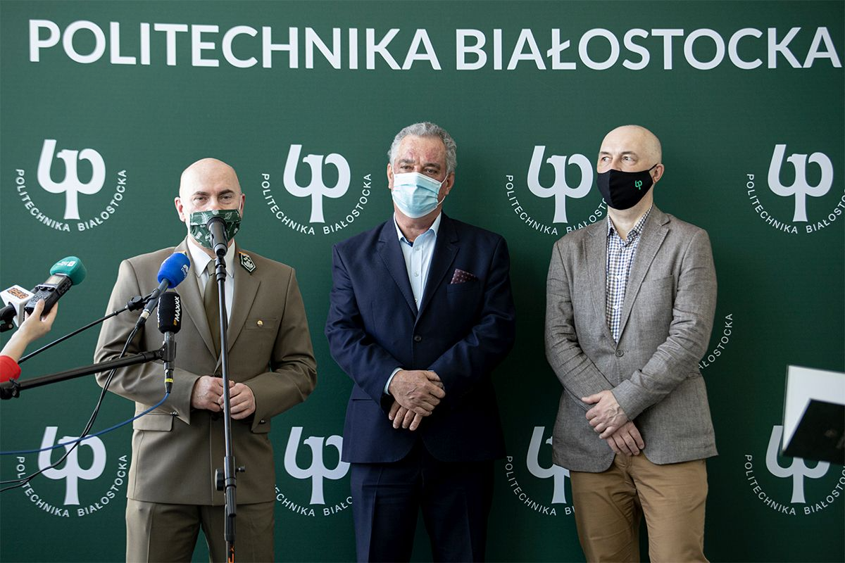 Trzech mężczyzn stoi na tle zielonej ścianki Politechniki Białostockiej