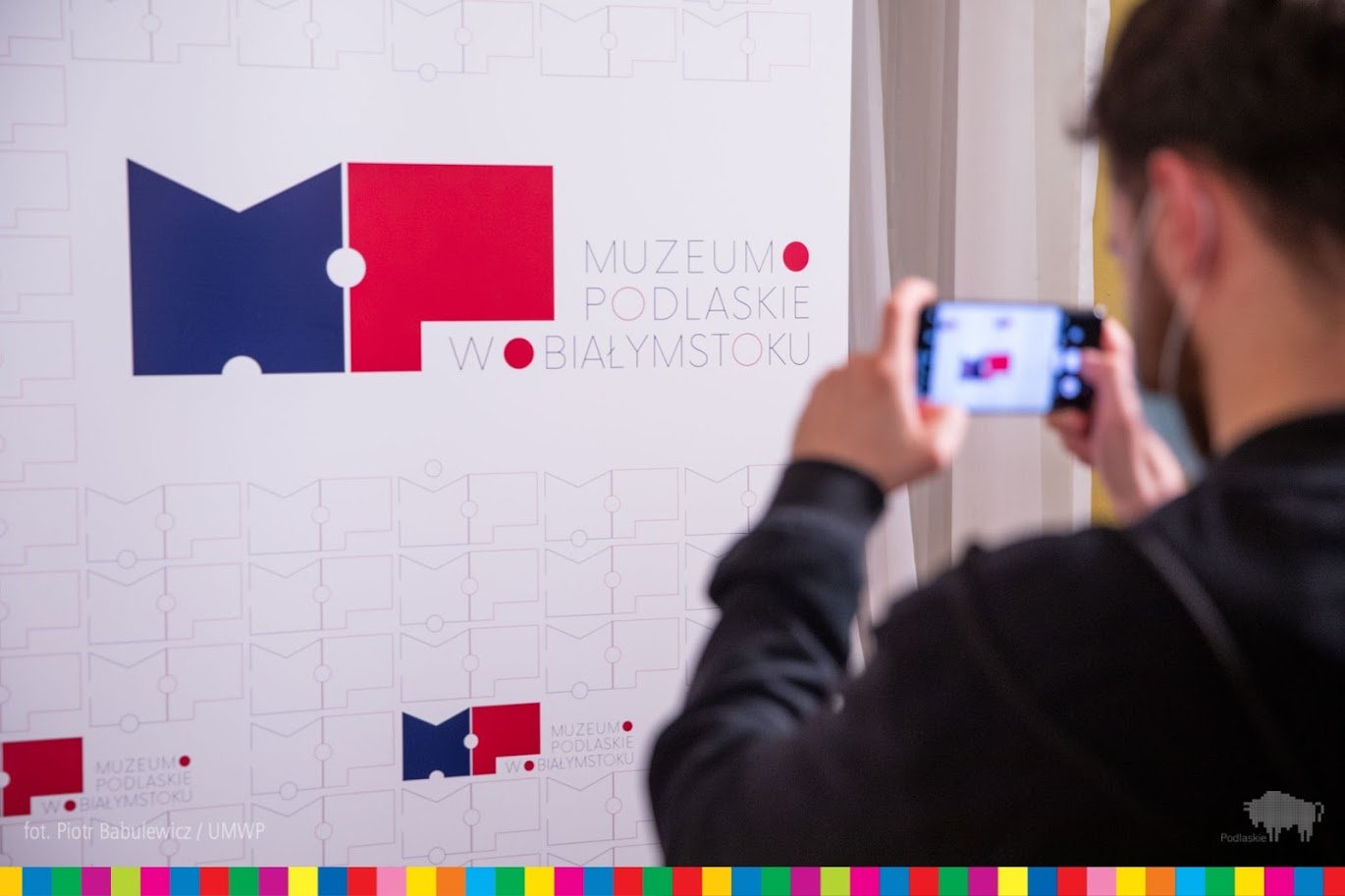 Chłopak robi zdjęcie banera prezentującego nowy logotyp Muzeum Podlaskiego w Białymstoku