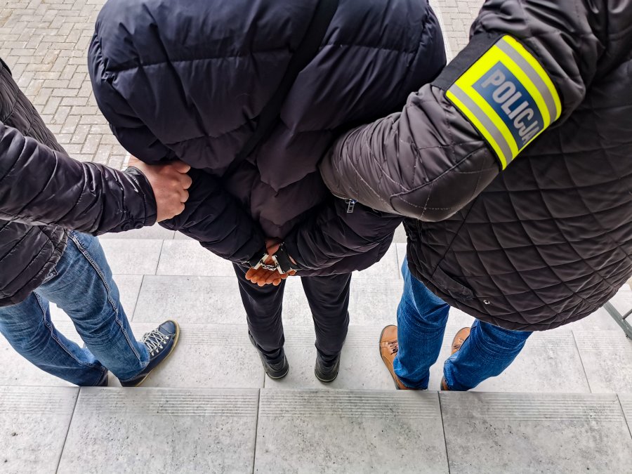 Dwaj policjanci trzymają skutego kajdankami mężczyznę