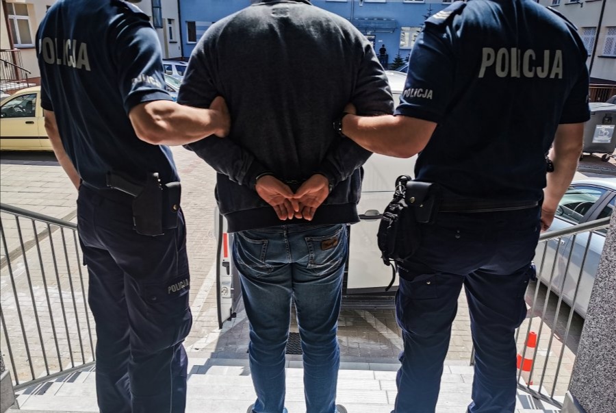 Dwaj policjanci trzymają skutego kajdankami mężczyznę