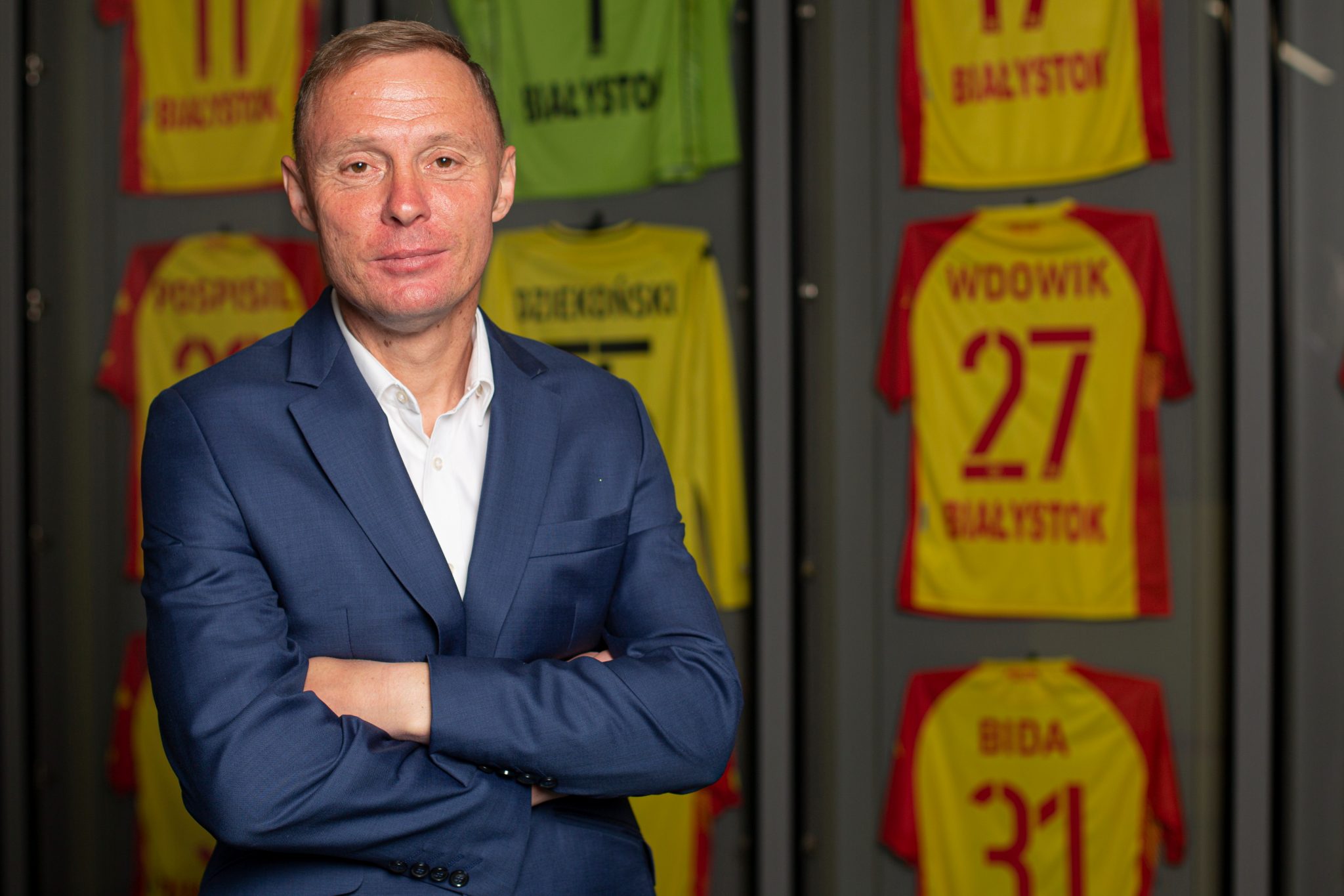 Trener Ireneusz Mamrot stoi na tle ściany, na której wiszą koszulki zawodników Jagiellonii