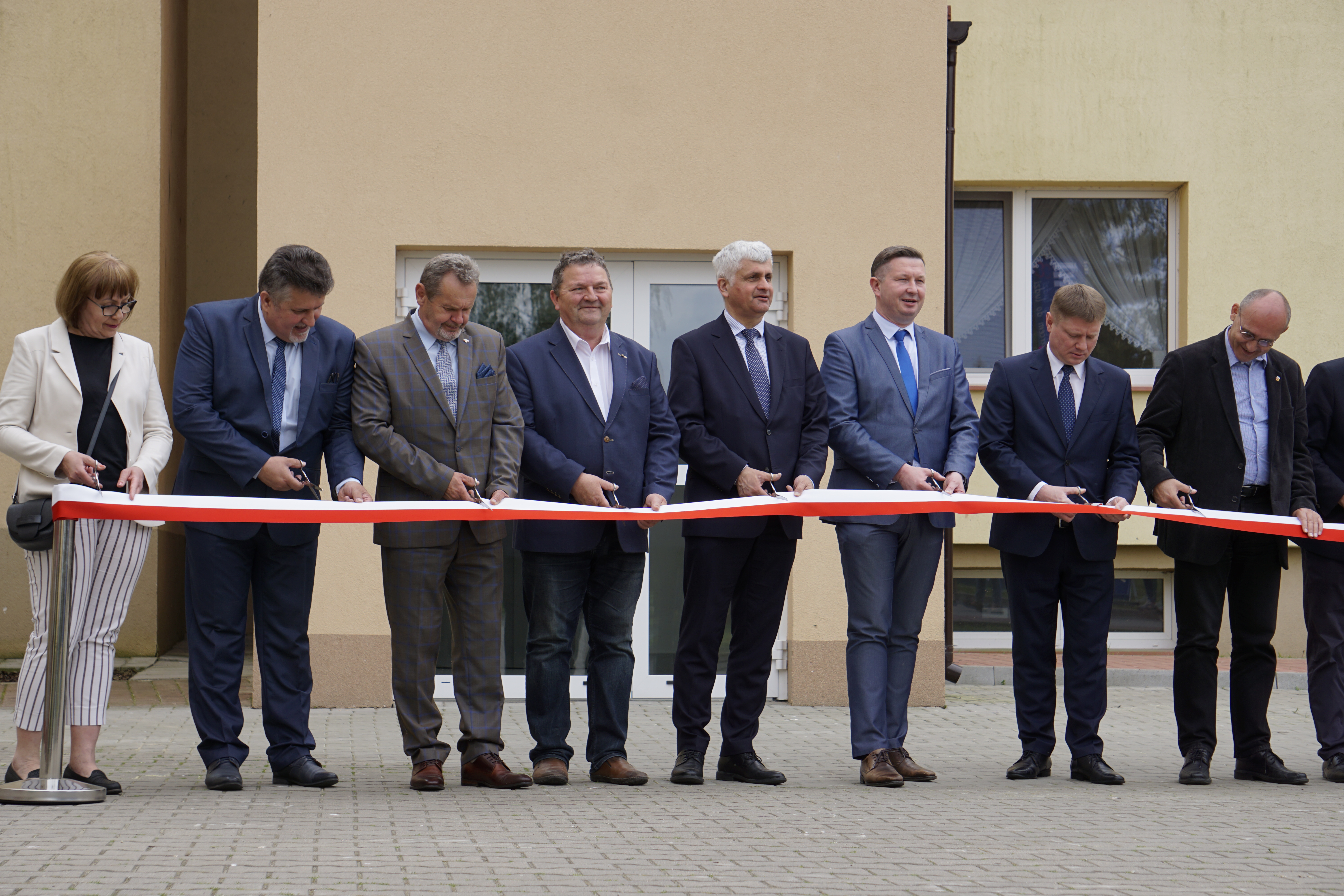Mężczyźni stojący w rzędzie przecinają biało - czerwoną wstęgę