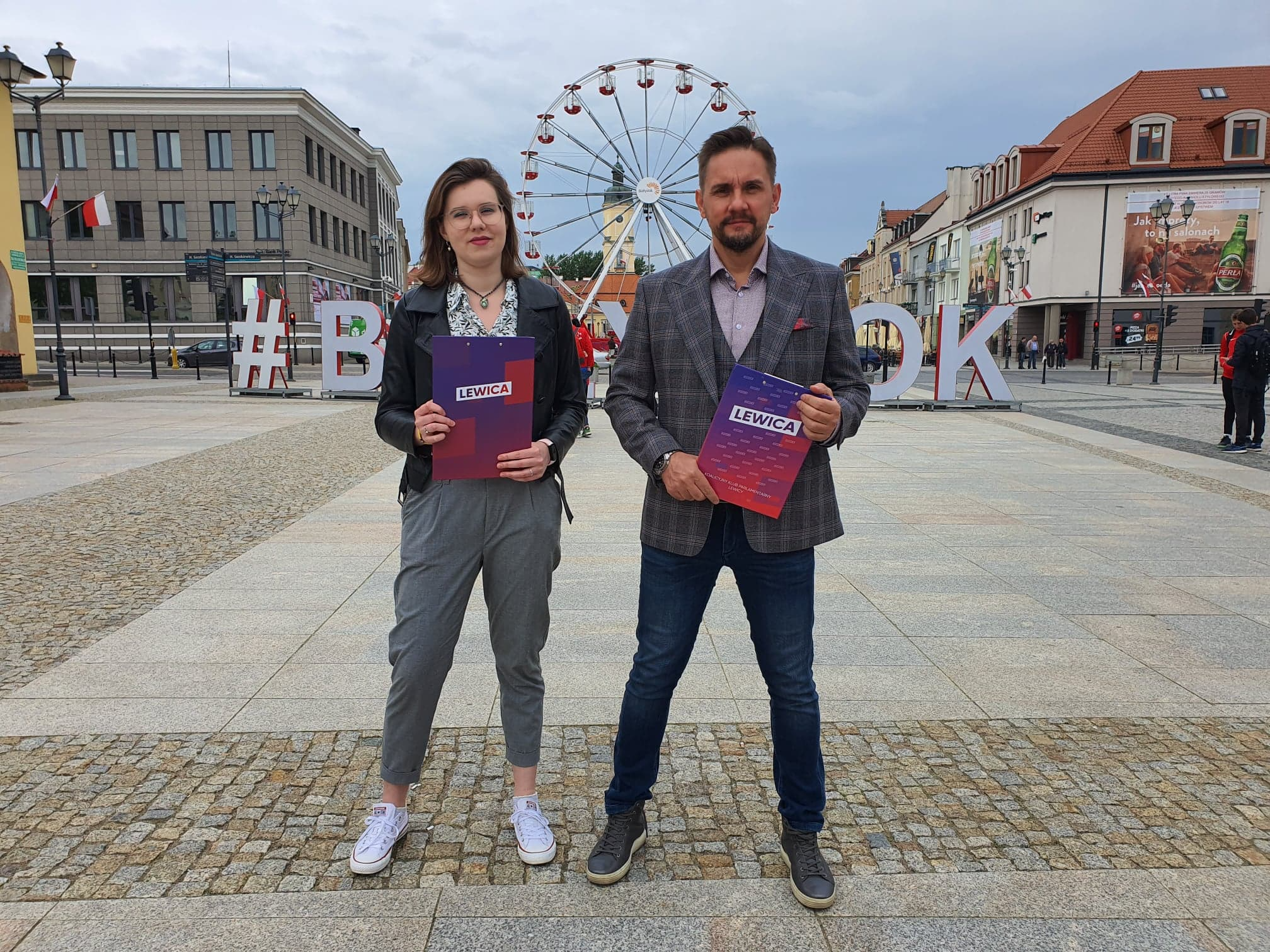 Kobieta i mężczyzna stoją na placu na Rynku Kościuszki w Białymstoku za nimi znajduje się młyńskie koło
